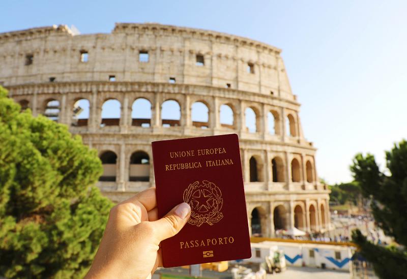 Hand holding Italian passport in front of Colosseum in Rome