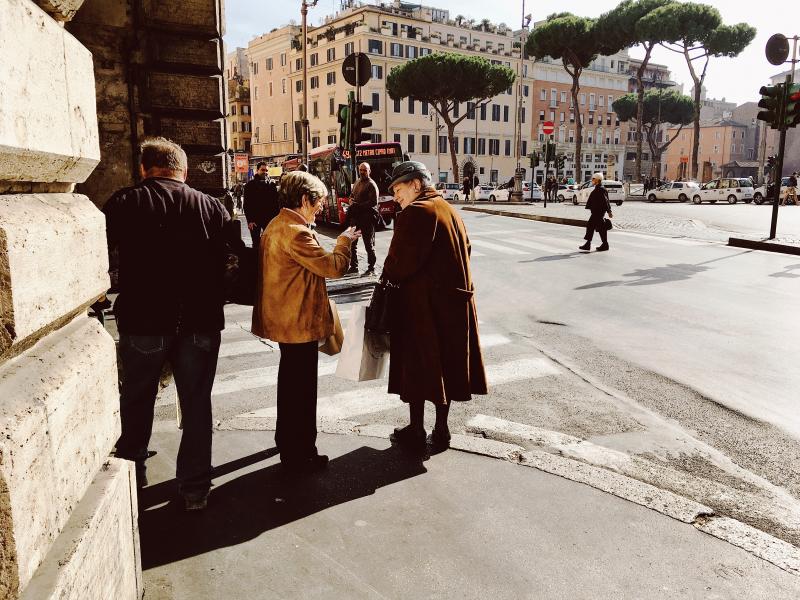 two older Italian women converse on a street corner in Rome with a bus in the background
